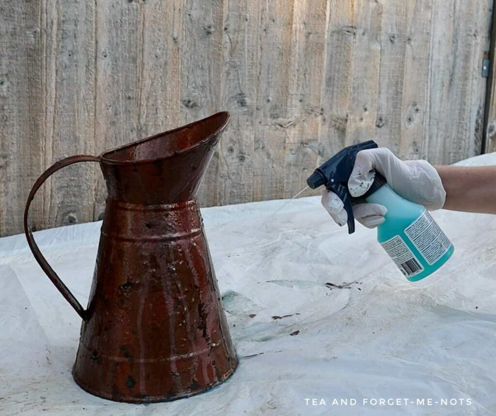 Applying patina spray to metal jug
