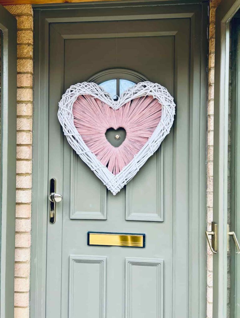 Image shows heart shaped yarn wreath on green front door.