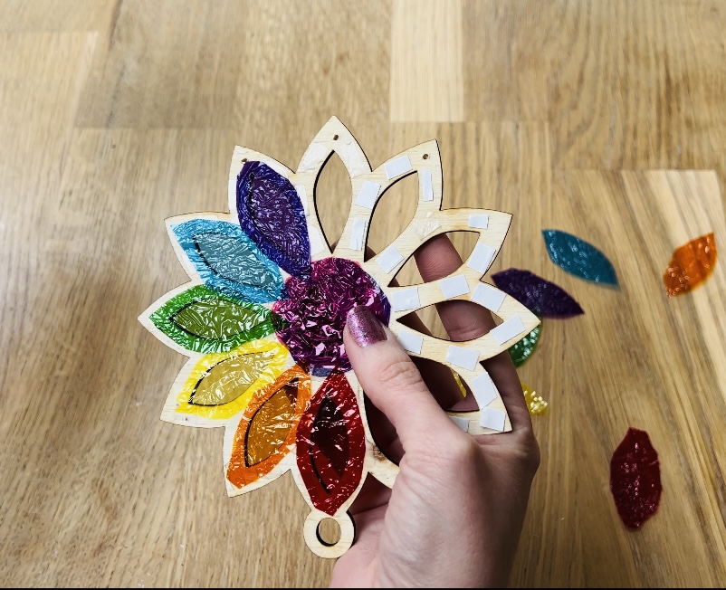 image shows using double-sided tape to attach candy wrappers to plywood.