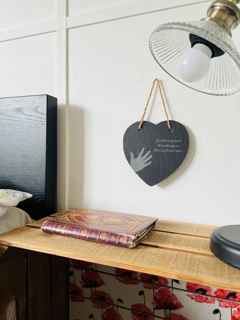 image shows engraved slate heart hanging on a wall next to a bed.