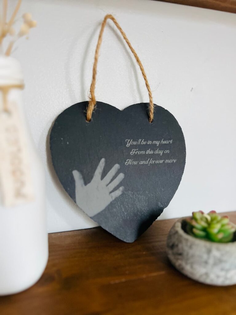 image shows engraved slate heart on a shelf with a bottle and candle.
