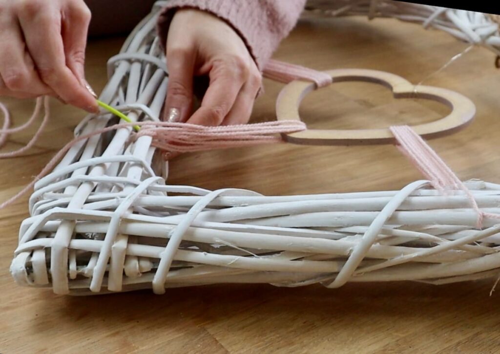 Image shows threading yarn through wicker heart.