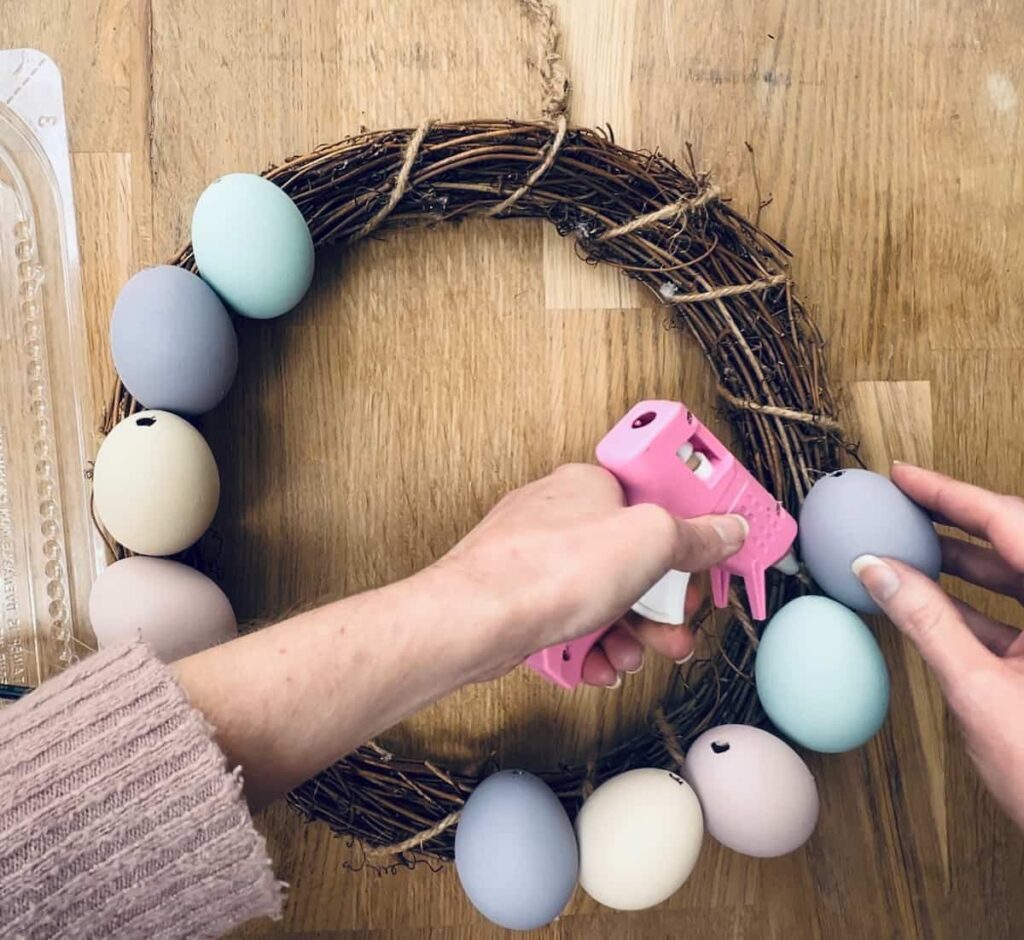 image shows attaching eggs to a wreath with a hot glue gun.