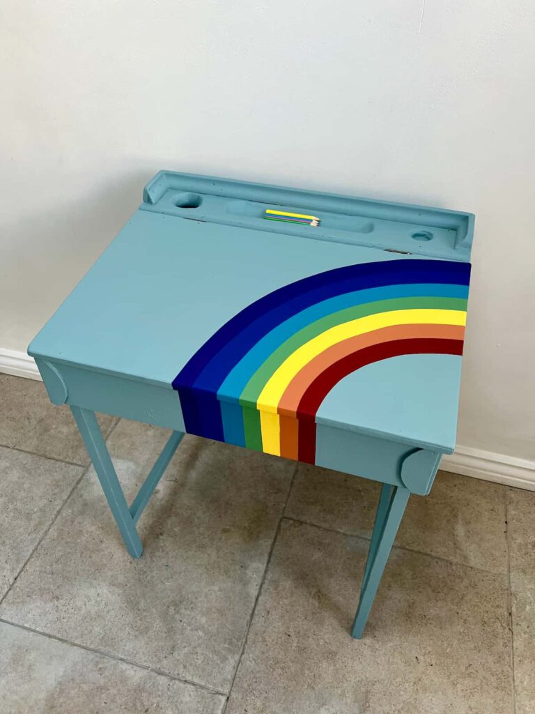 image shows blue painted desk painted with curved lines of a rainbow.
