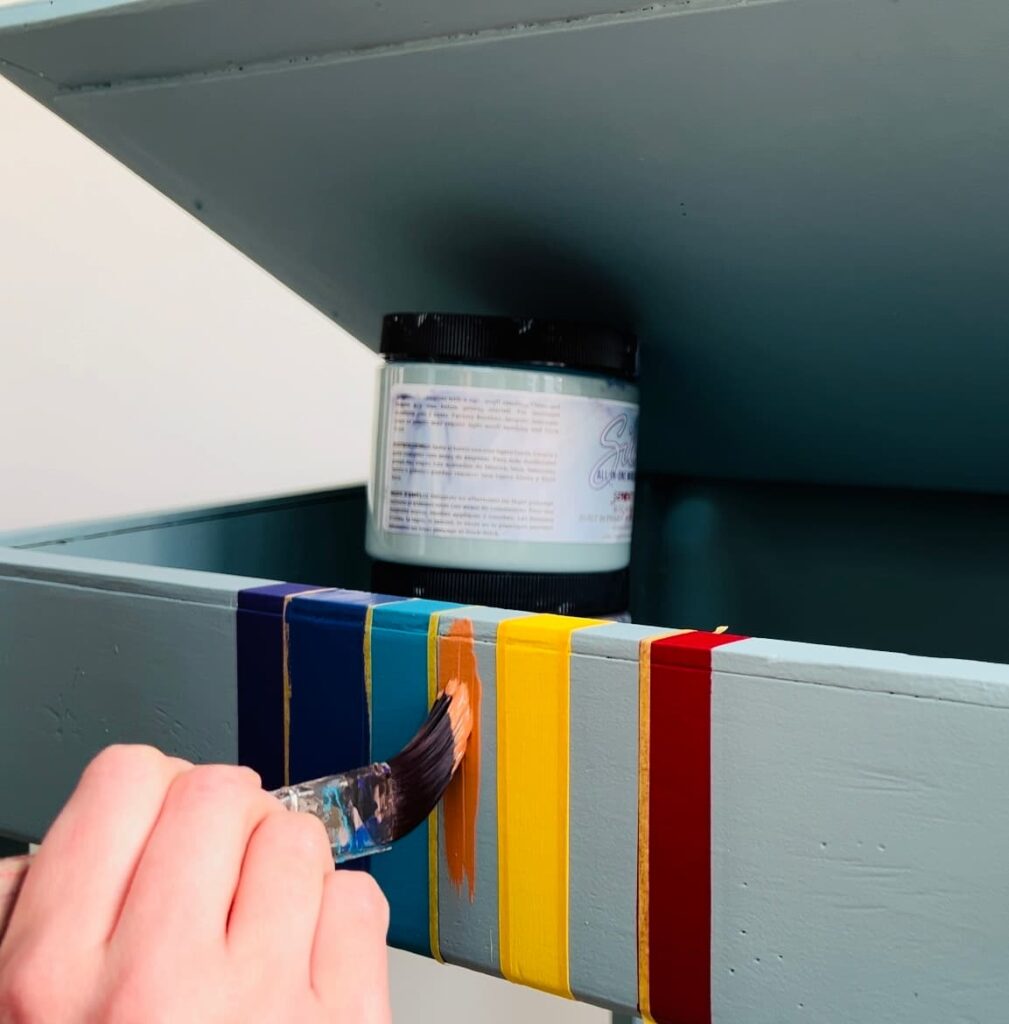 image shows painting orange stripe of rainbow on desk.