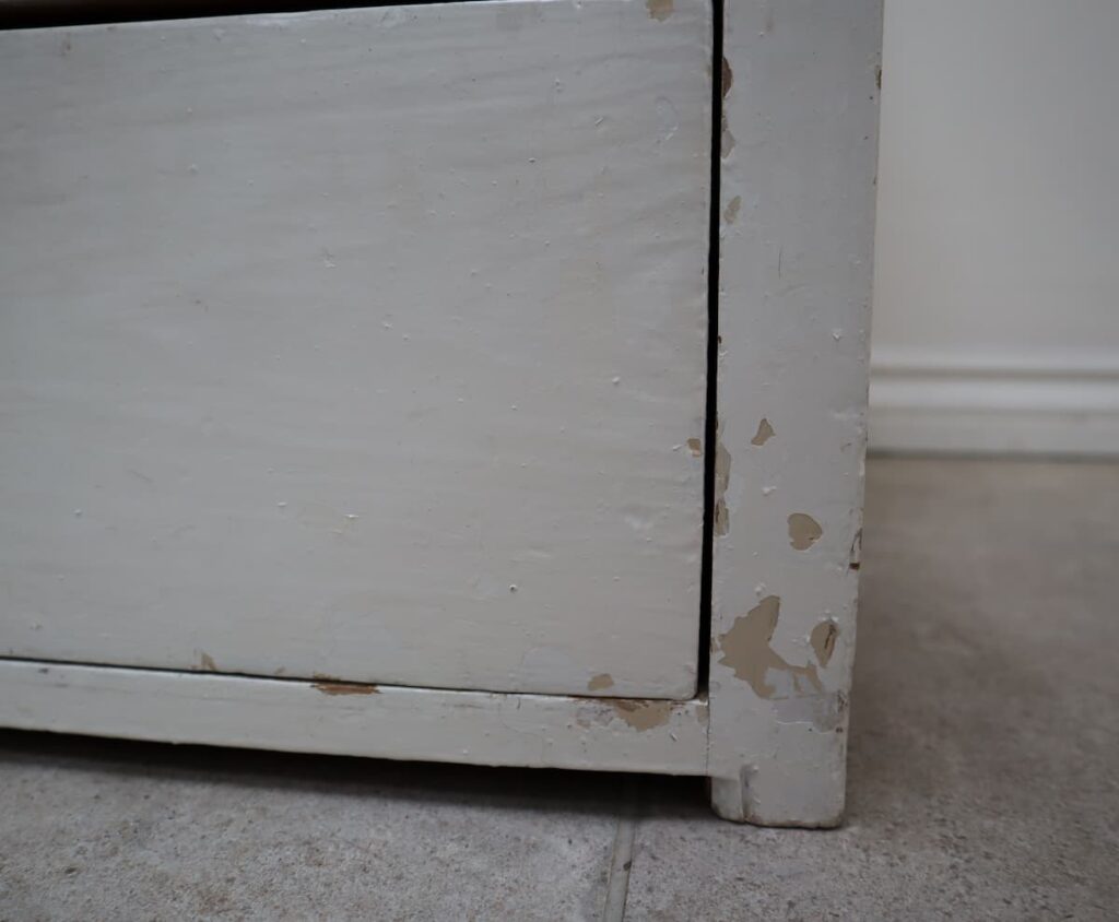 image shows corner of a chest of drawers with flaking paint.