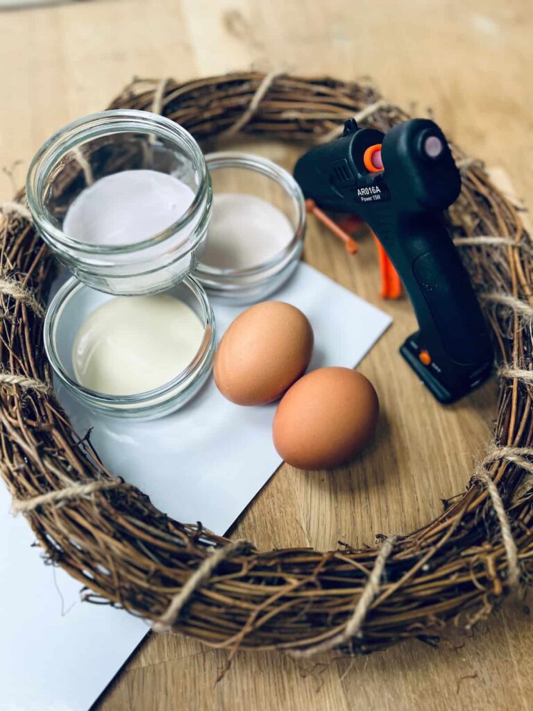 image shows wreath, eggs, paint and glue gun on a table.