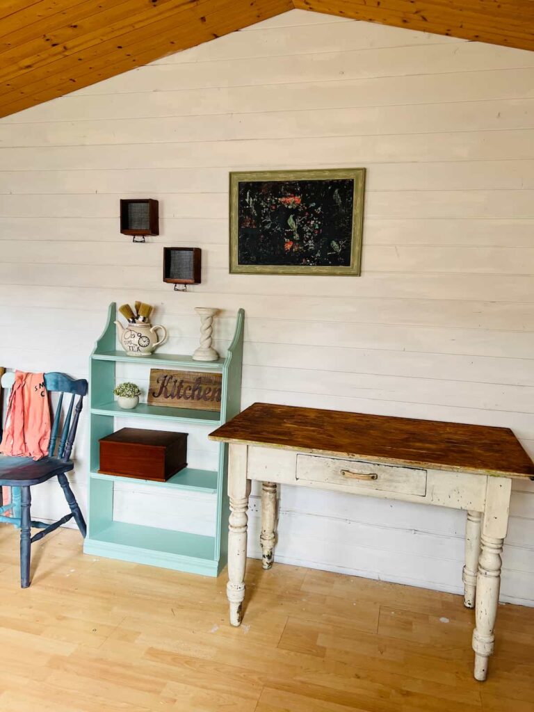 image shows shed painted white with table and shelves.