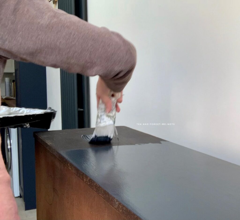 Using a brush on the top to paint wood furniture black with Black Sands 