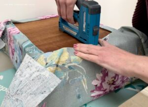 Stapling the final side to reupholster an old footstool