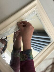 Removing excess paint with a razor blade to Update a wooden mirror