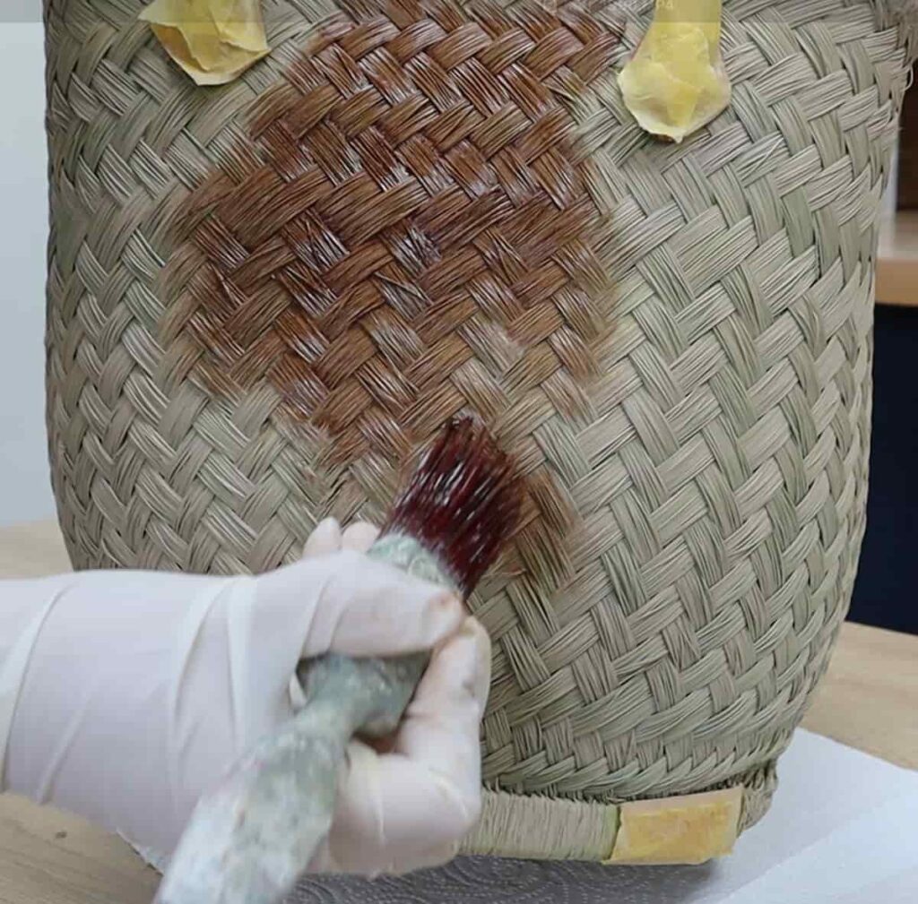image shows applying brown stain to basket with brush.