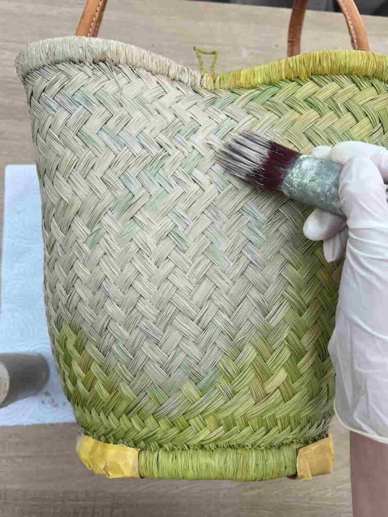 green basket bag with natural stain being applied with brush.