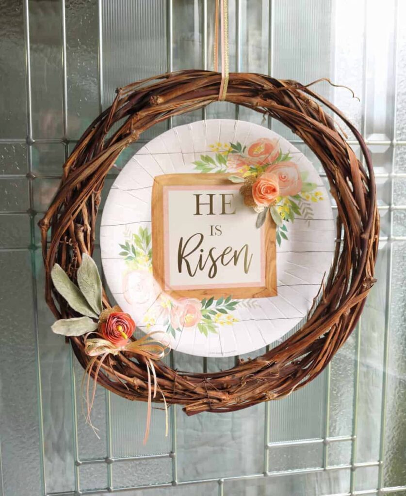 image shows grapevine wreath with he is risen message.
