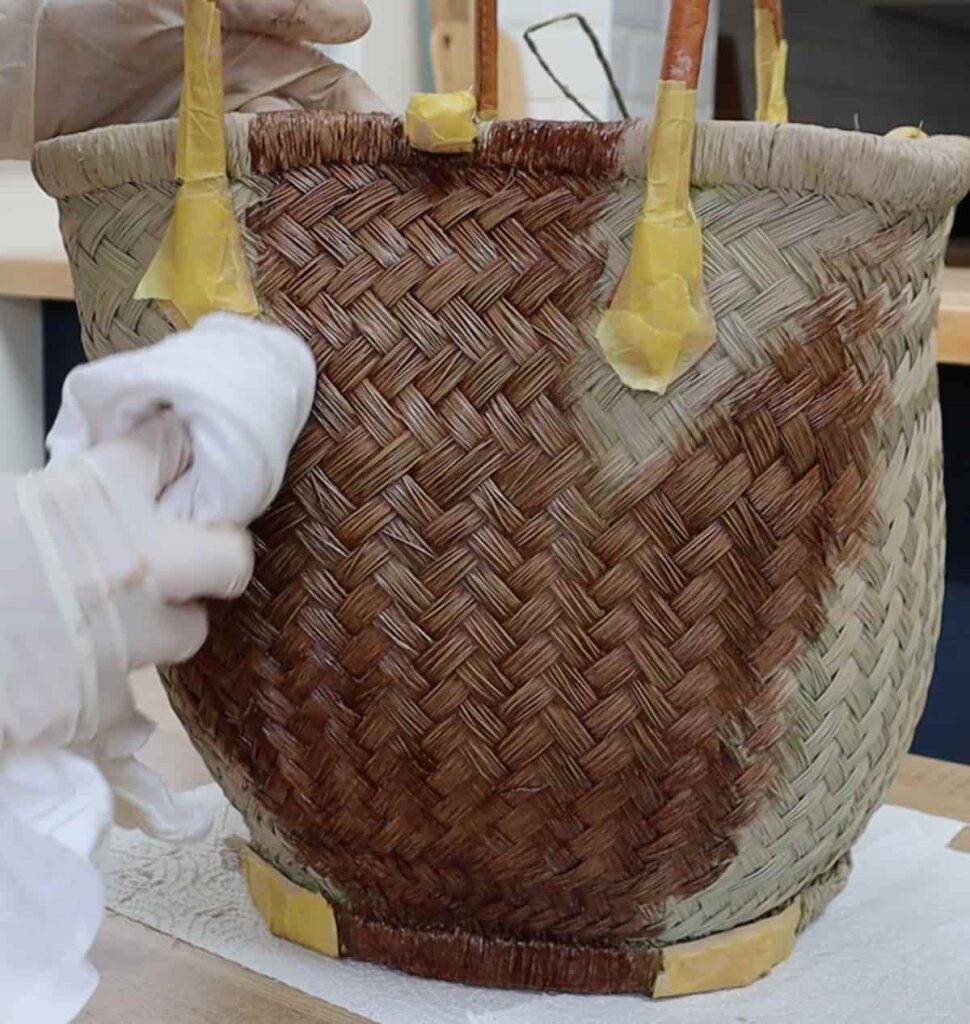 image shows removing excess stain from a basket with a rag.